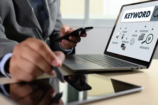 Businessman using smartphone and laptop, with keyword and graphics displayed on the laptop