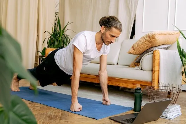 Taking an online fitness class using a laptop and yoga mat